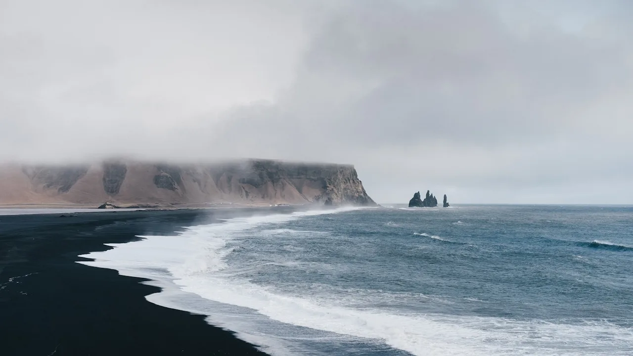 Aerial view of Icelandic black sand beach with turquoise waves crashing against basalt sea cliffs