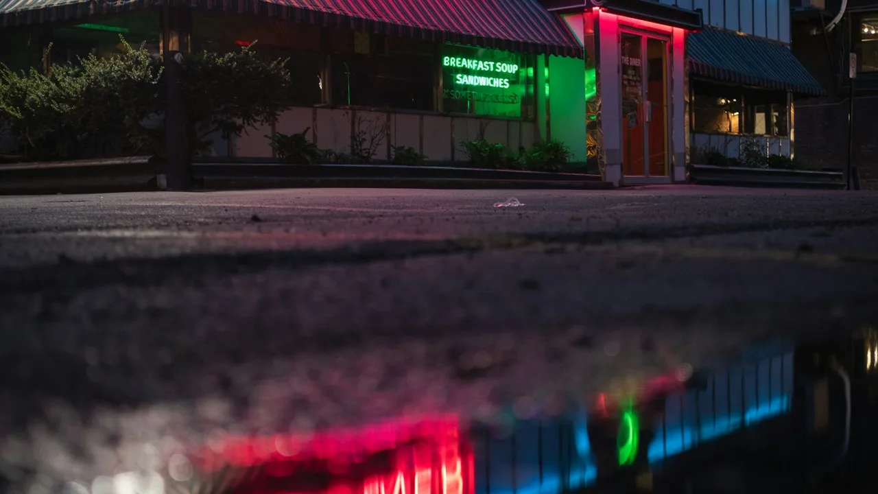 Cinematic American diner at 3 AM with warm incandescent light glowing onto a rain-slicked midnight street
